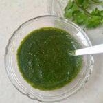 Green chutney filled in a glass bowl with a spoon
