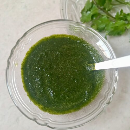 Green chutney filled in a glass bowl with a spoon