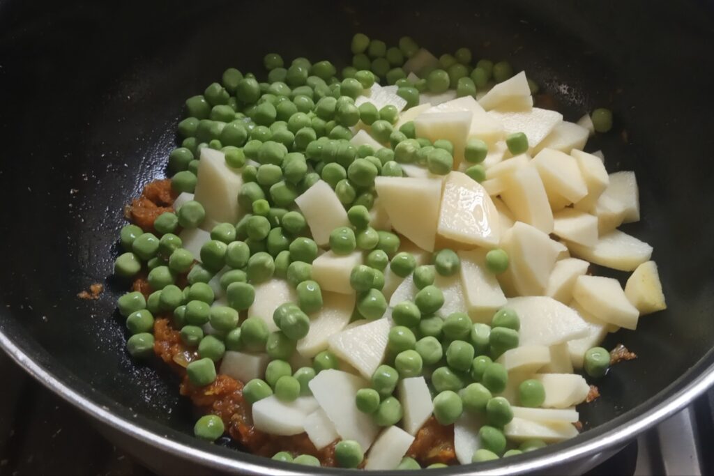 adding chopped potato and green peas to the masala