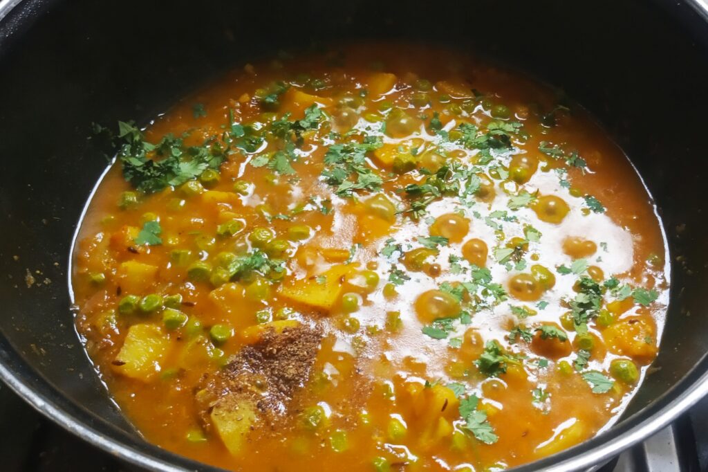 adding masala and coriander leaves  to the potato peas curry