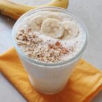 glass of oats banana smoothie with sliced bananas on top
