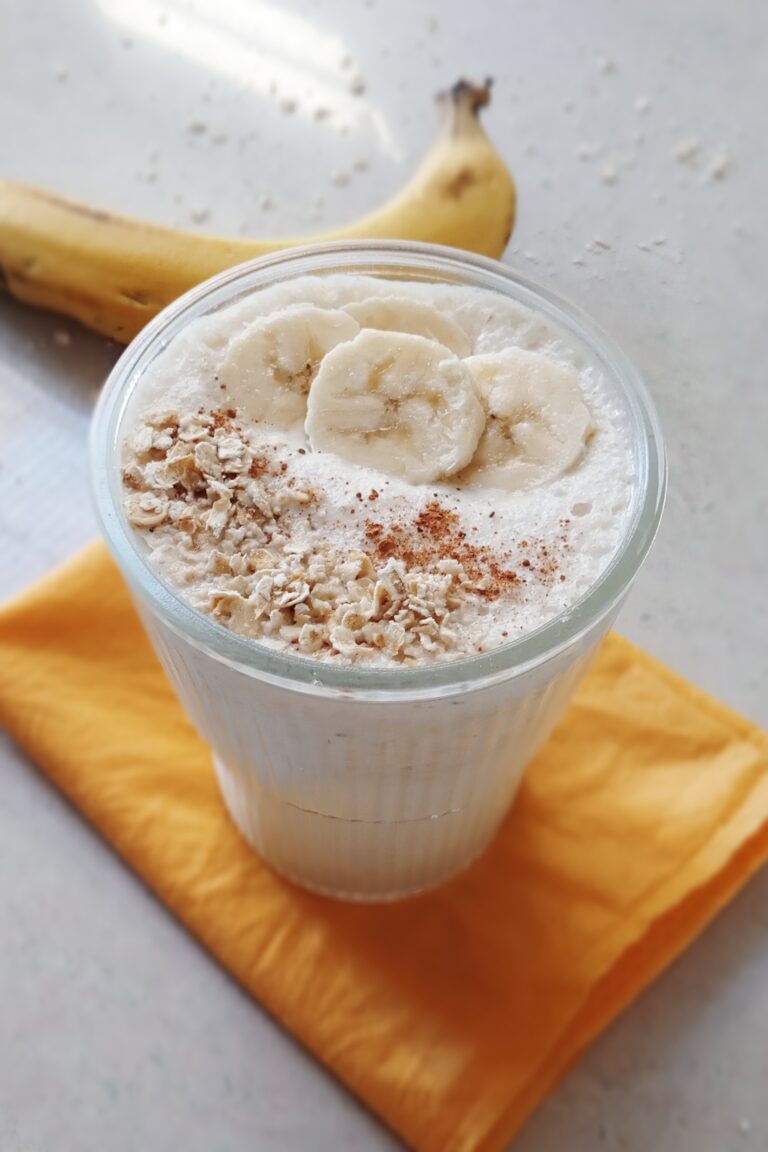 glass of oats banana smoothie with sliced bananas on top