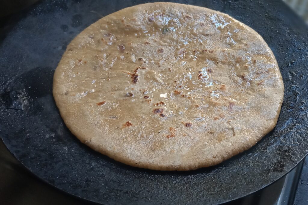 applying ghee on the sattu paratha and its edges