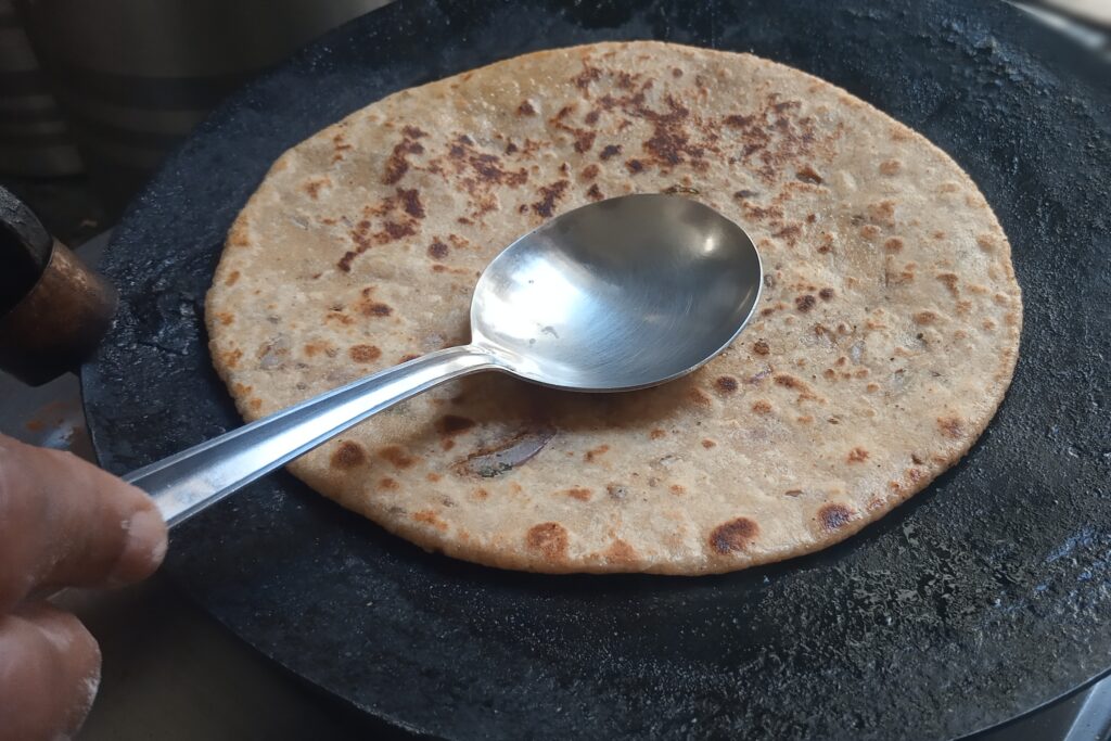 pressing paratha with spatula for even cooking